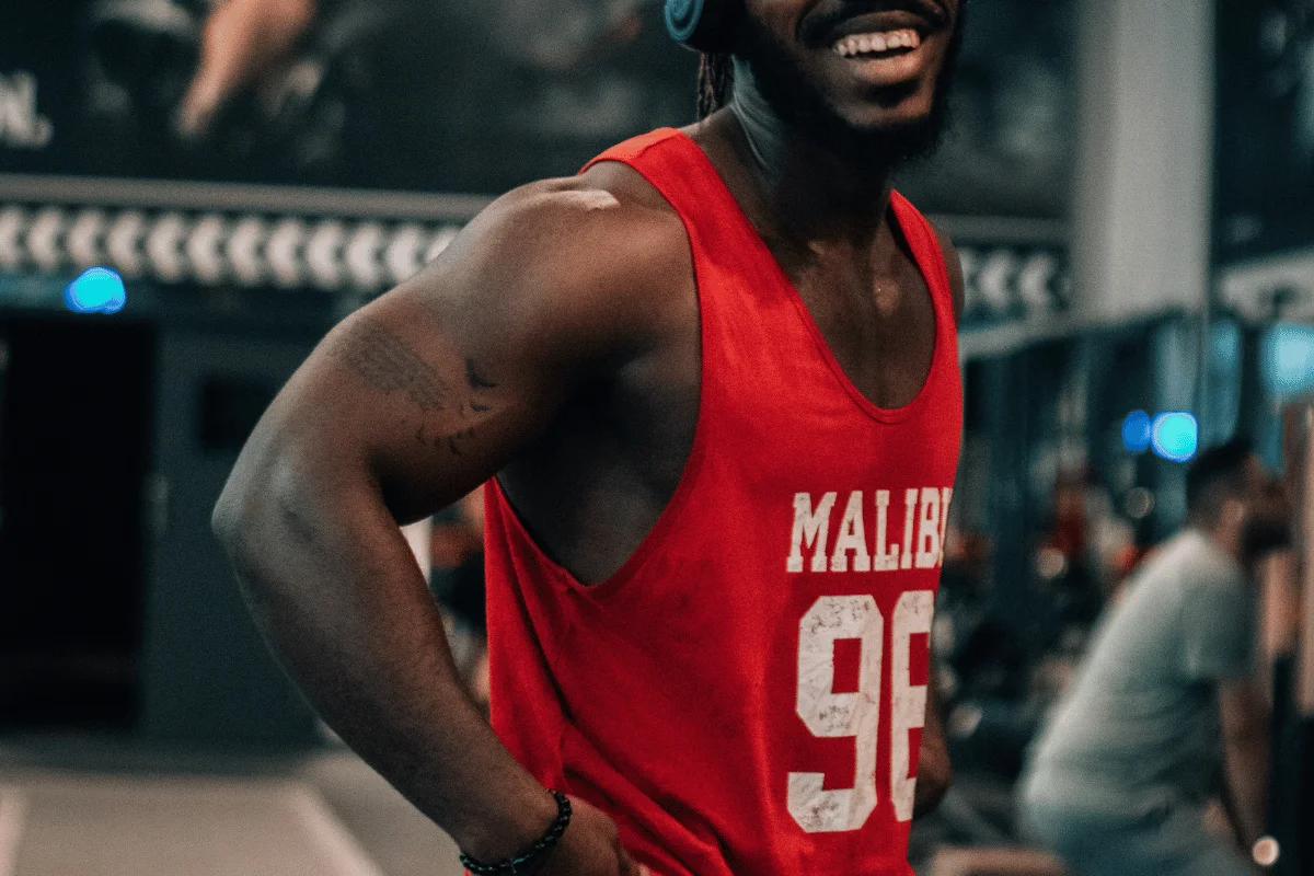 Smiling man in a red tank top during a gym workout.