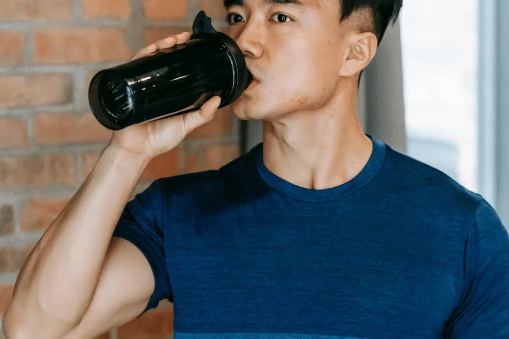 Man drinking from a black protein shaker bottle in a blue shirt.