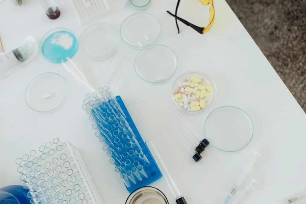 Overhead view of a lab setup with petri dishes, test tubes, pipettes, and assorted pills.