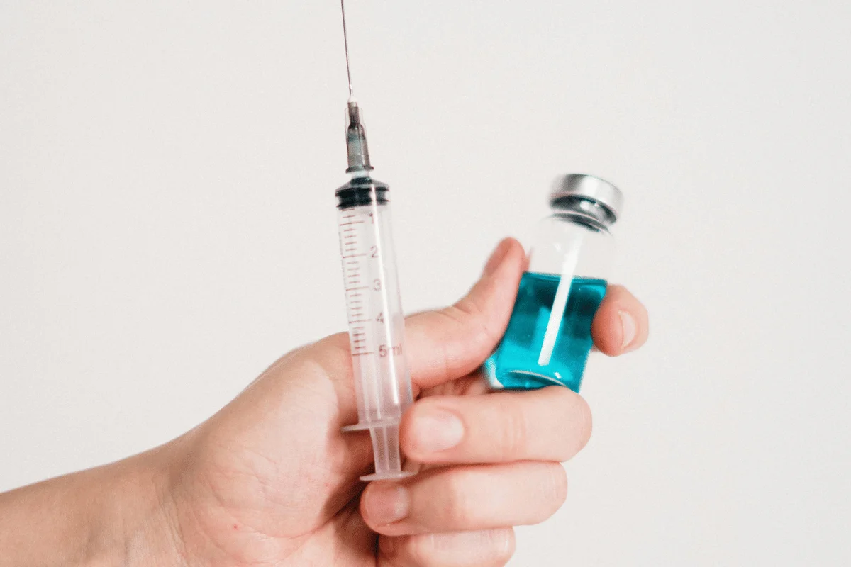 Hand holding a syringe and a vial with blue liquid.