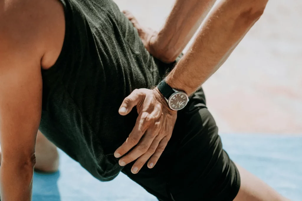 Close-up of a person's hand on their hip, wearing a dark tank top and a wristwatch.