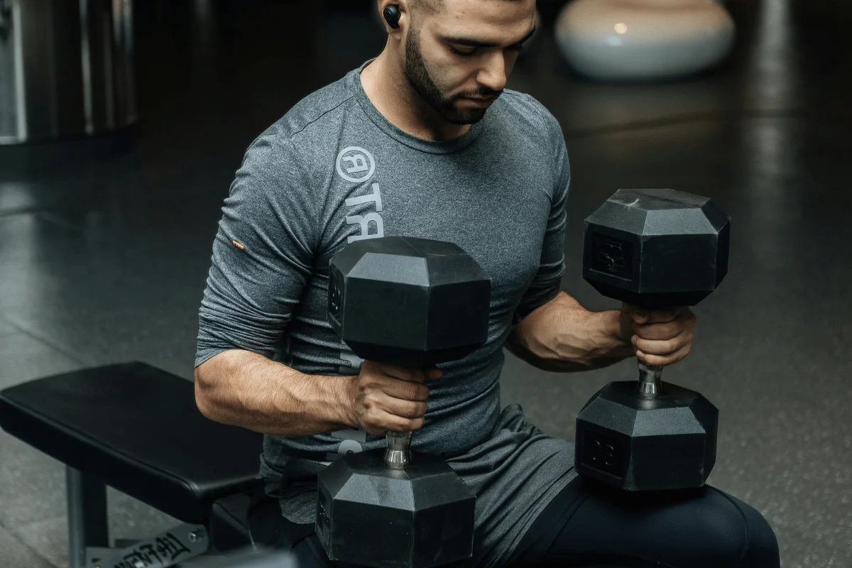 A person in a gym lifting heavy dumbbells while seated on a bench.