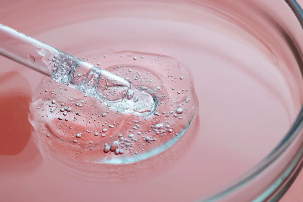 Pipette dropping liquid onto a petri dish with pink substance and bubbles.