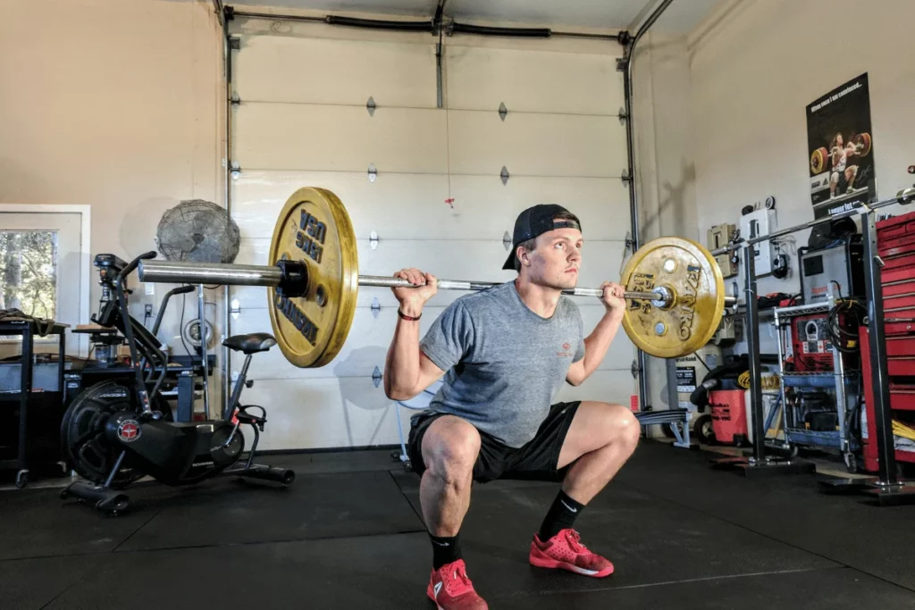 Man performing a squat with a barbell and weights in a home gym setting.