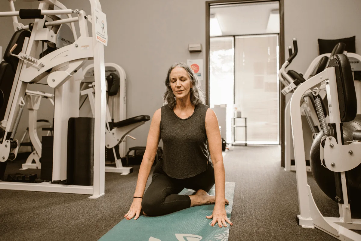 Person doing a seated twist yoga pose on a mat in a gym.