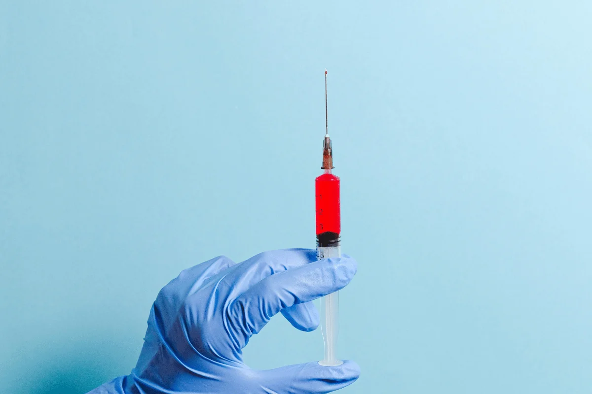 Gloved hand holding syringe filled with red liquid on a blue background.