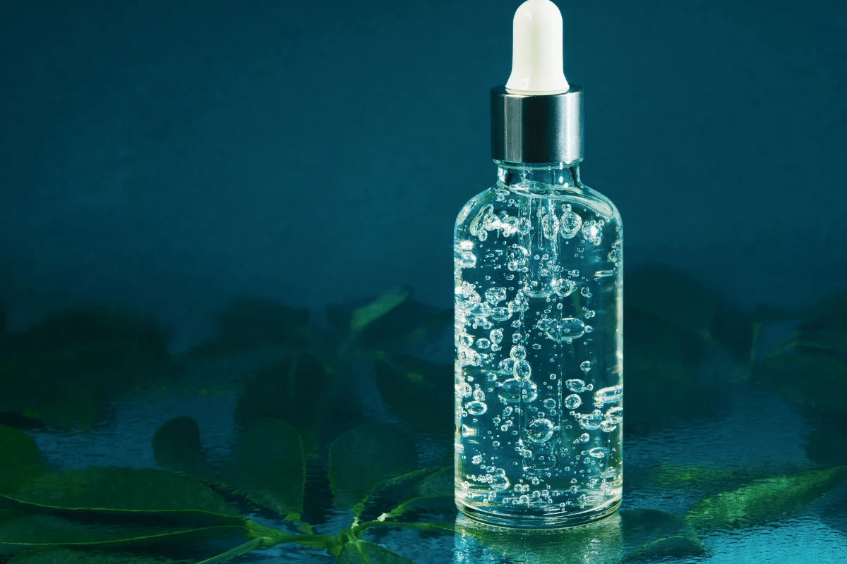 A dropper bottle with clear liquid and bubbles on a blue background with green leaves.