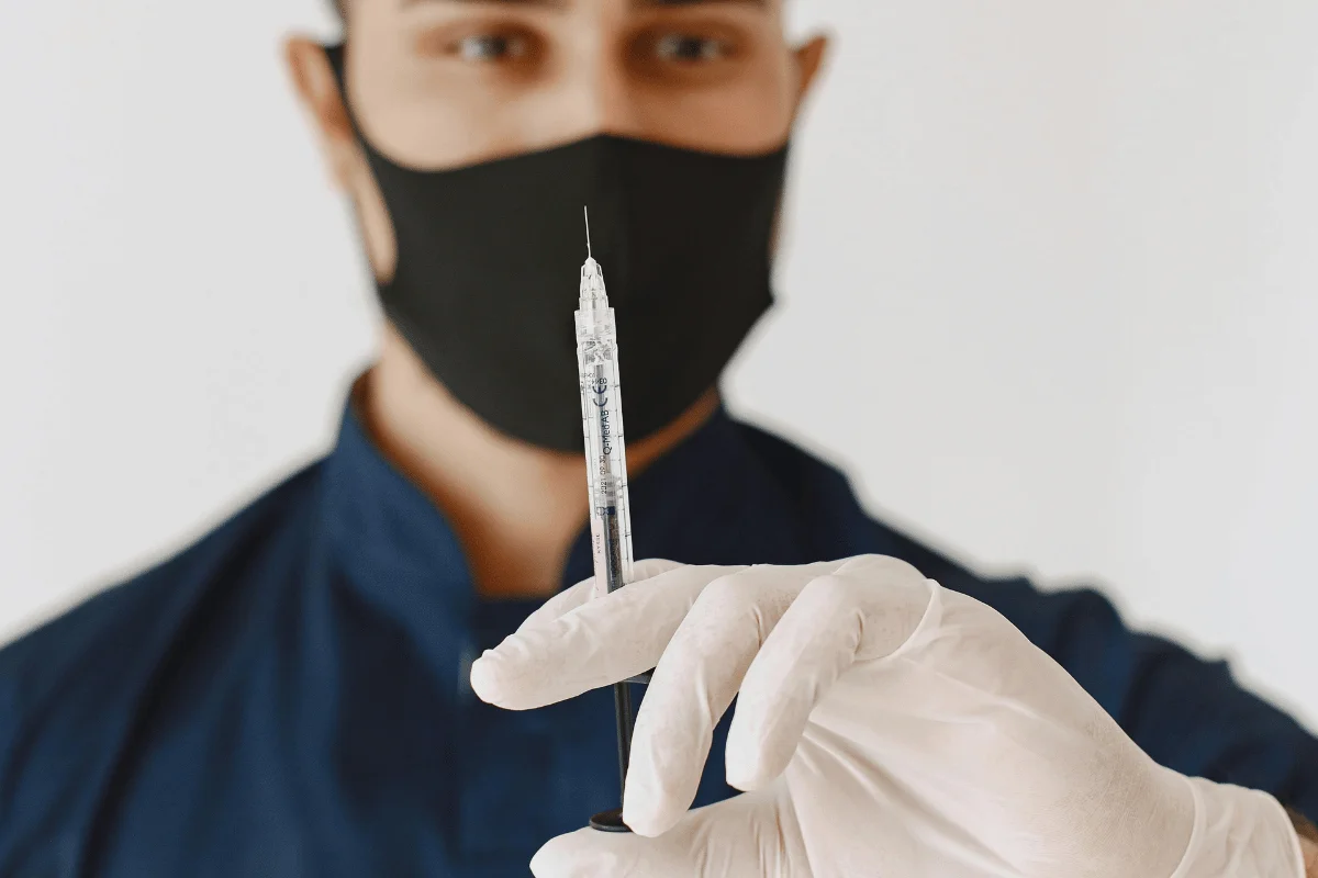 Person in blue holding a syringe, wearing white gloves.