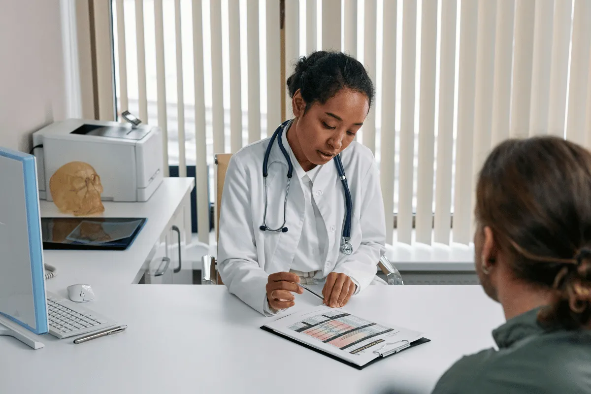 Female doctor reviewing medical charts with a patient in a clinical office setting.