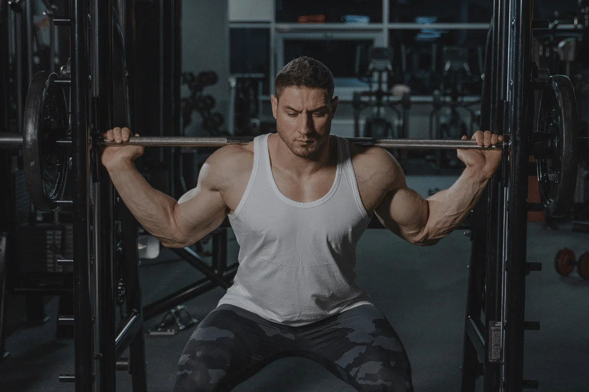 Muscular man performing a squat exercise with a barbell, focusing on lower body strength in a gym setting.