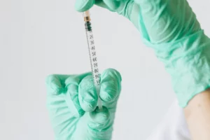 Close-up of hands in green gloves preparing a syringe for injection.