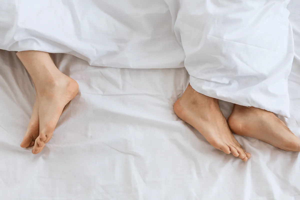 Two people resting in bed with feet exposed under a white blanket.