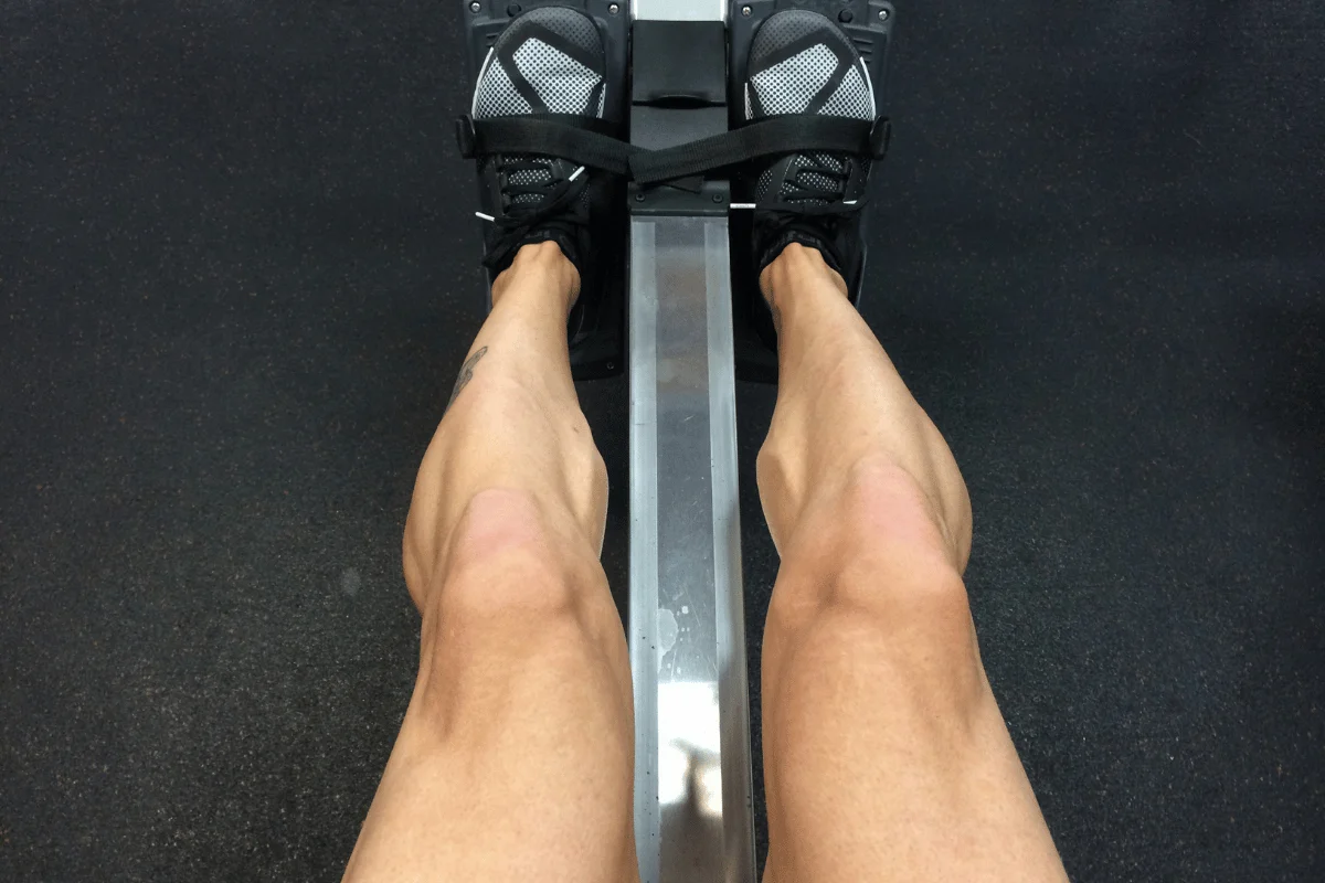 Close-up of legs during a rowing machine workout in a gym.