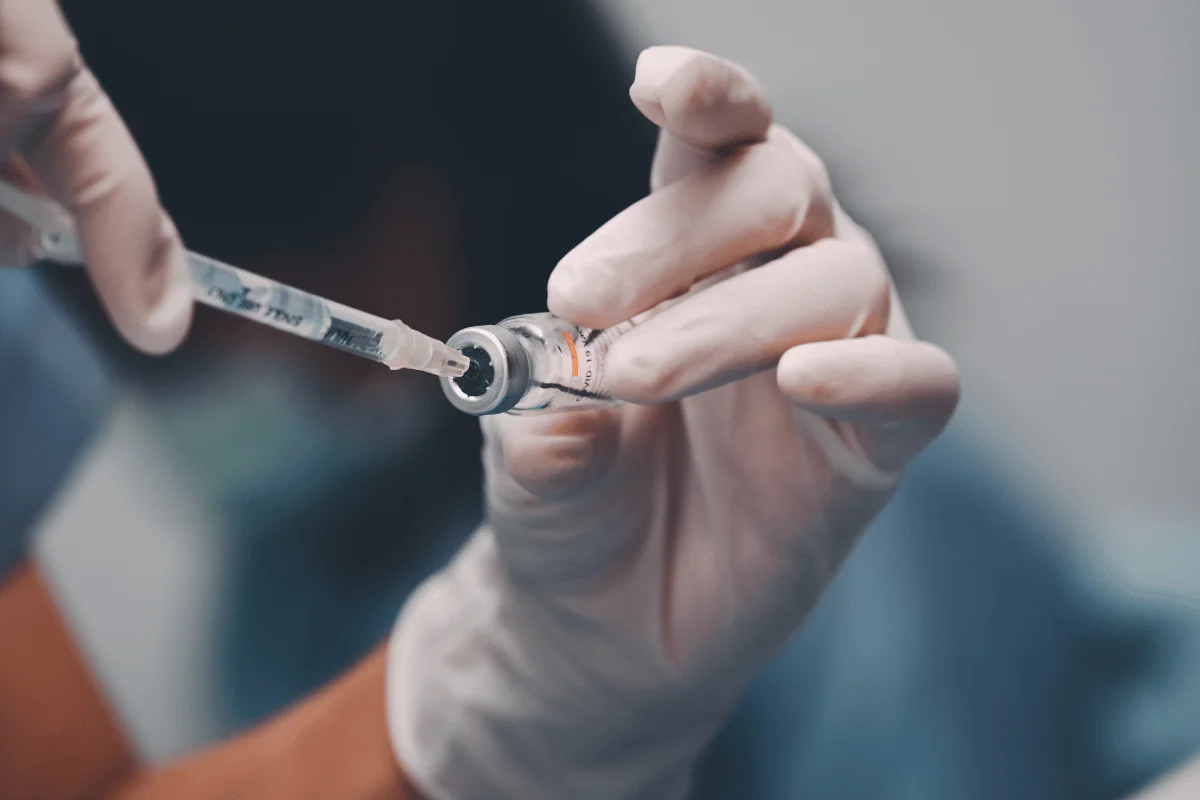 Healthcare worker drawing vaccine from vial into syringe, prepared for immunization.