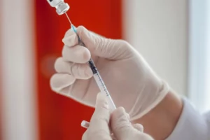 Healthcare professional in gloves preparing a syringe for injection.