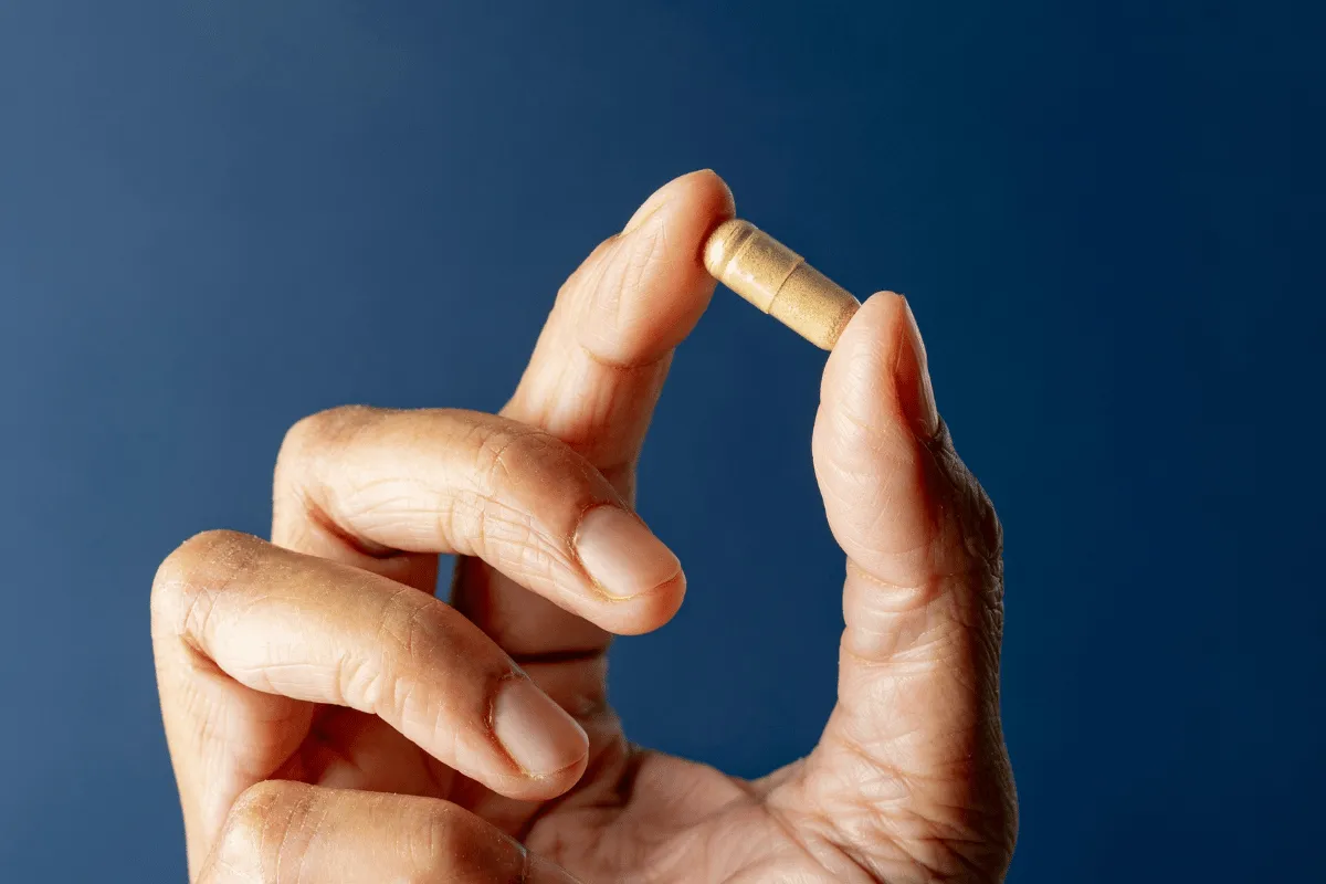 Close-up of a hand holding a single capsule pill against a blue background.