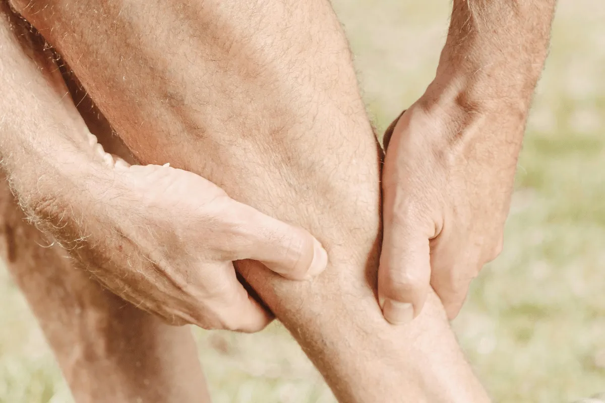 Close-up of a person holding their knee, experiencing pain or discomfort.