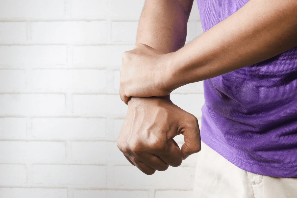 Person in a purple shirt holding their wrist, possibly due to wrist pain or injury, highlighting joint issues.