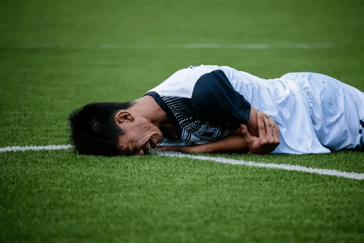 Injured soccer player holding arm and lying on grass field.