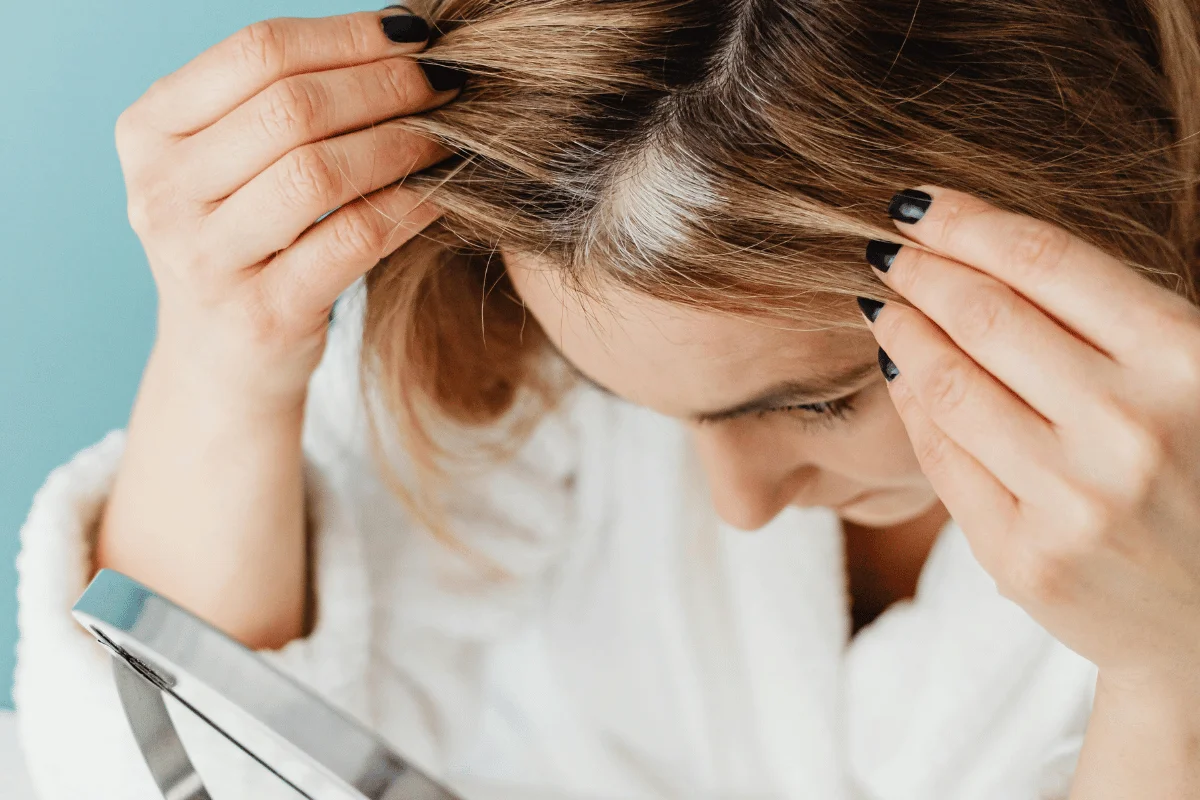 Person holding their hair with a mirror in hand against a blue background.