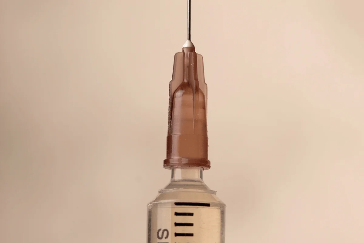 Syringe with a brown cap and needle, isolated on a plain background.