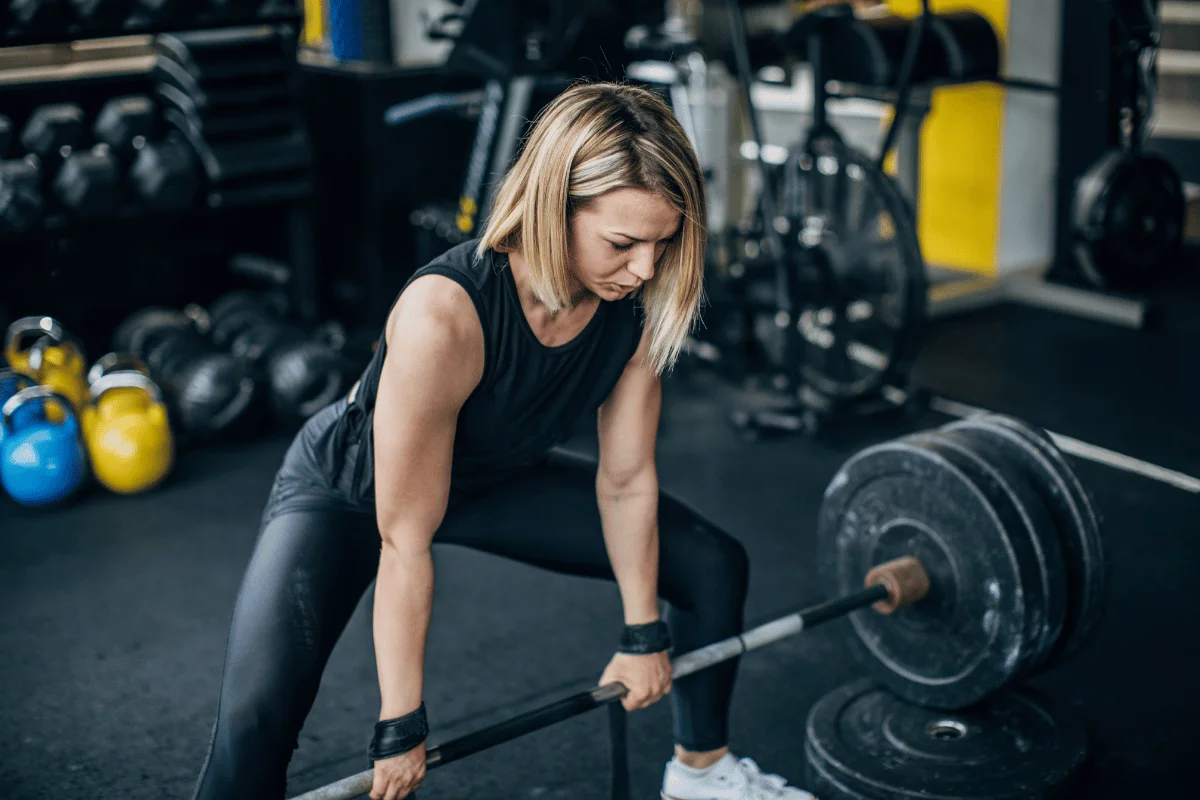 Woman performing a deadlift exercise with heavy barbell at the gym.