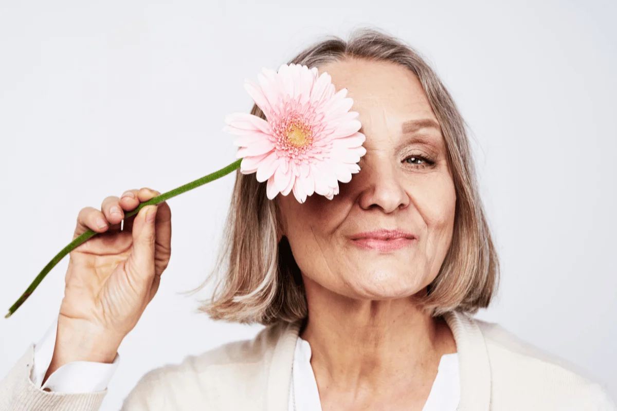 Person holding a pink gerbera daisy, wearing a white jacket, against a light background.