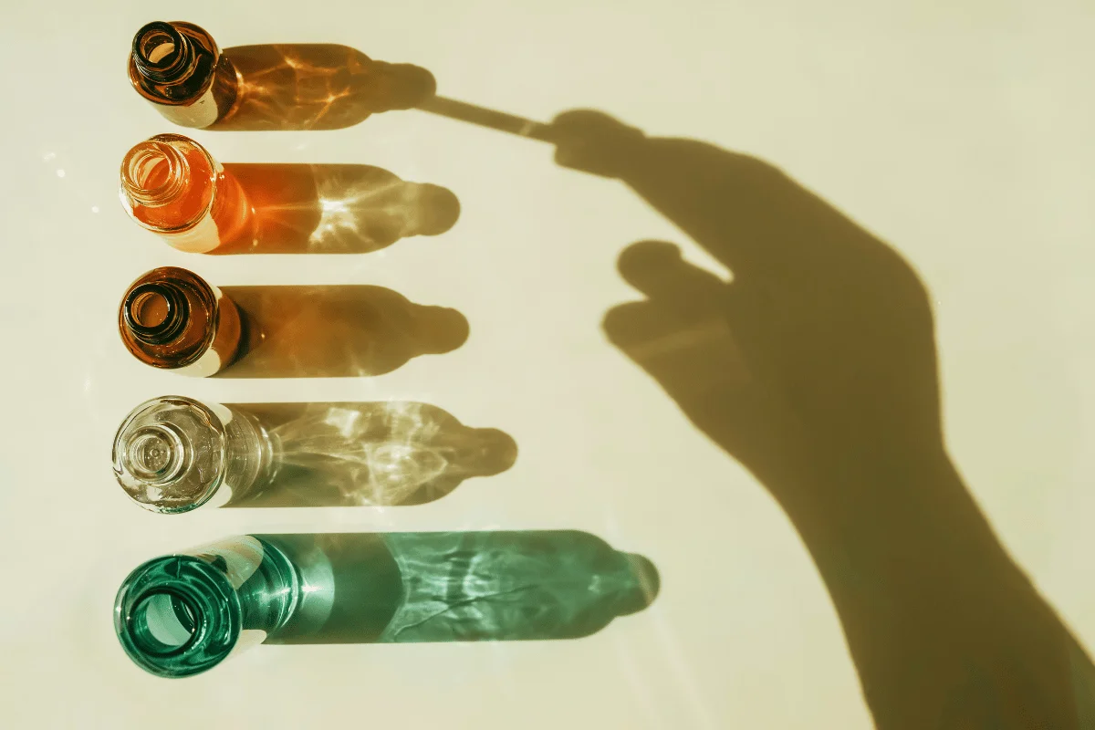 A shadow of a hand interacting with the light from multi-colored glass bottles on a surface.