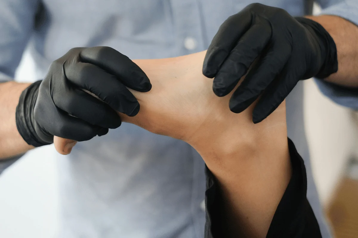 A person wearing black gloves examines the ankle of a patient during a foot check-up.