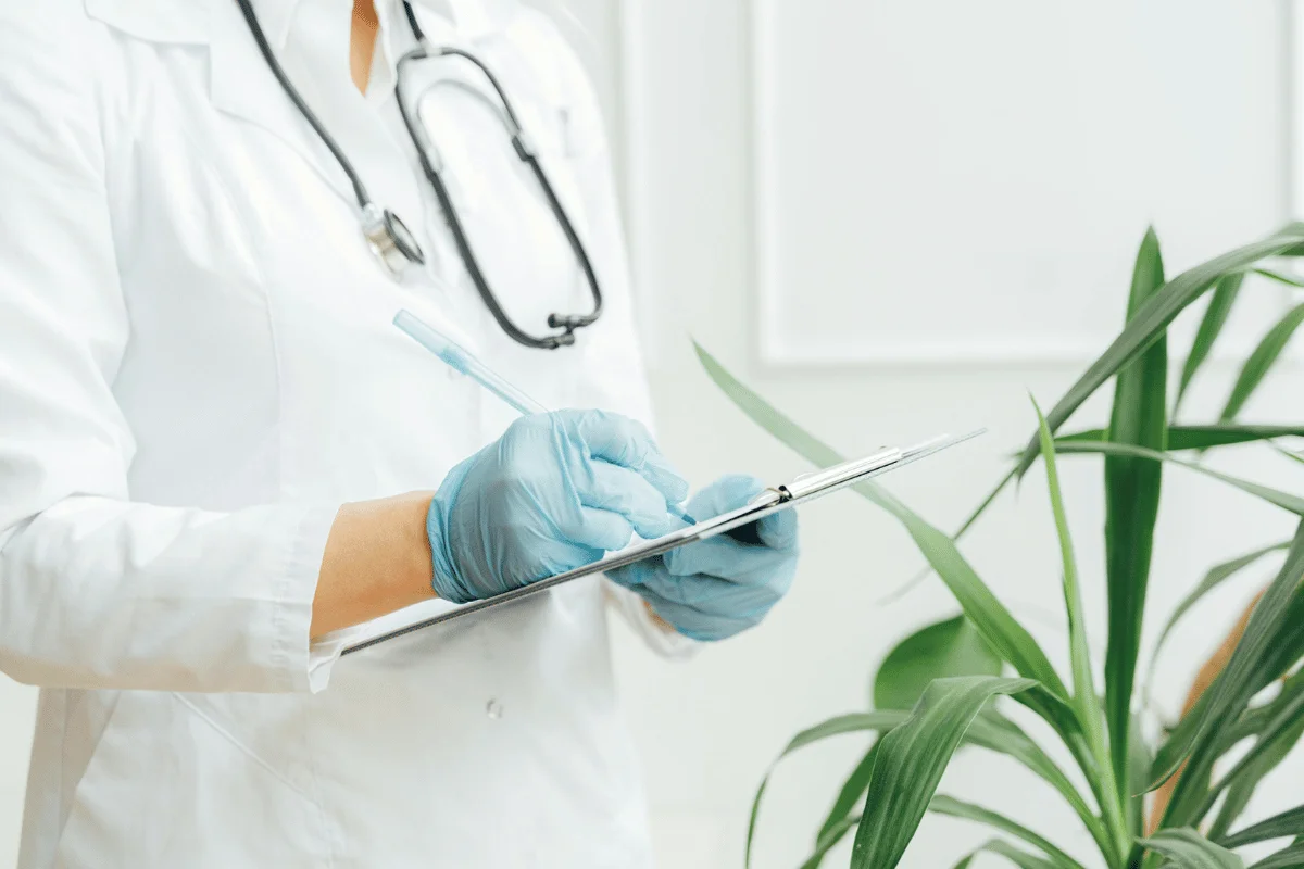 Healthcare professional wearing gloves, taking notes on a clipboard.