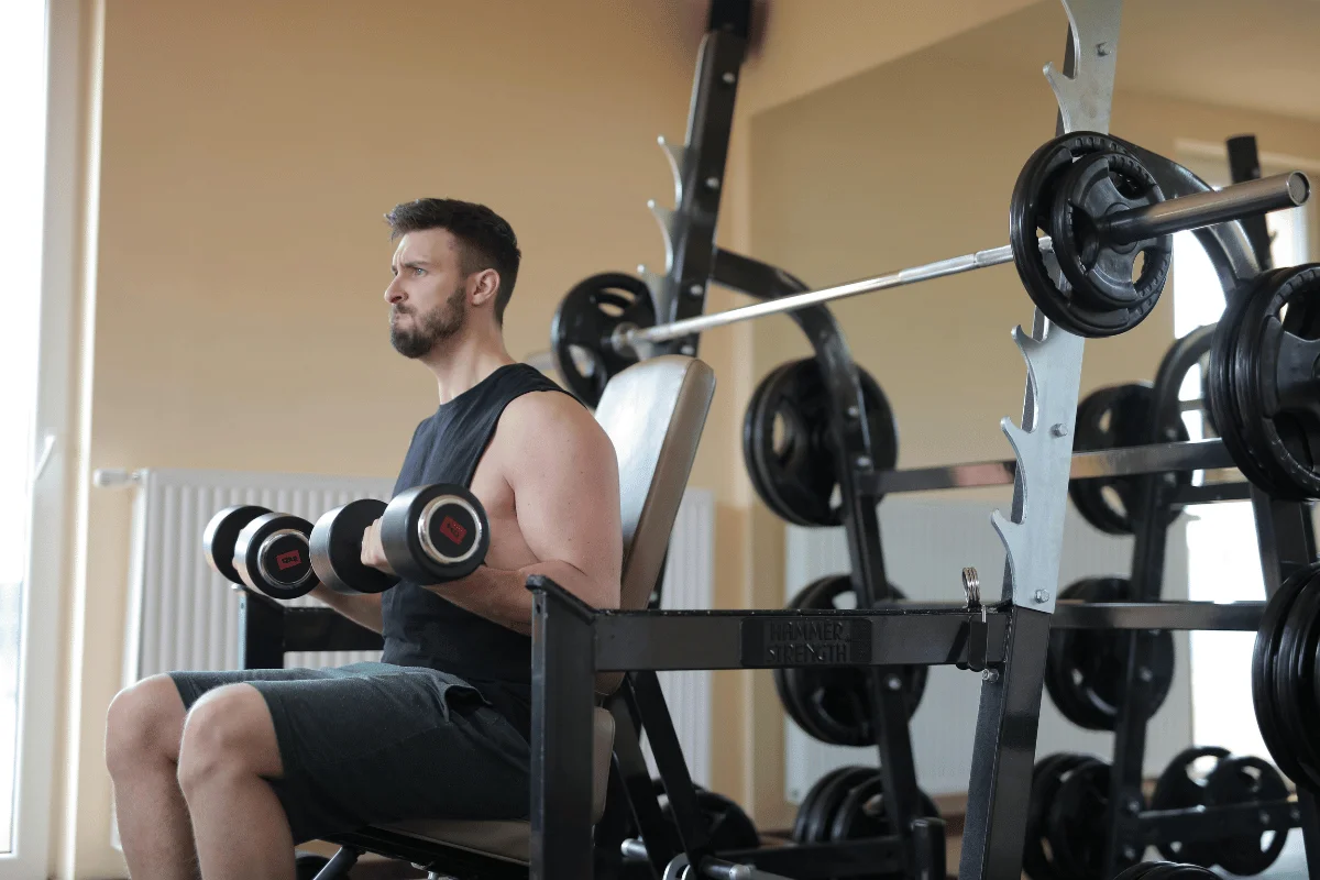 Man performing seated dumbbell curls in a gym, focusing on bicep strength training and muscle development.