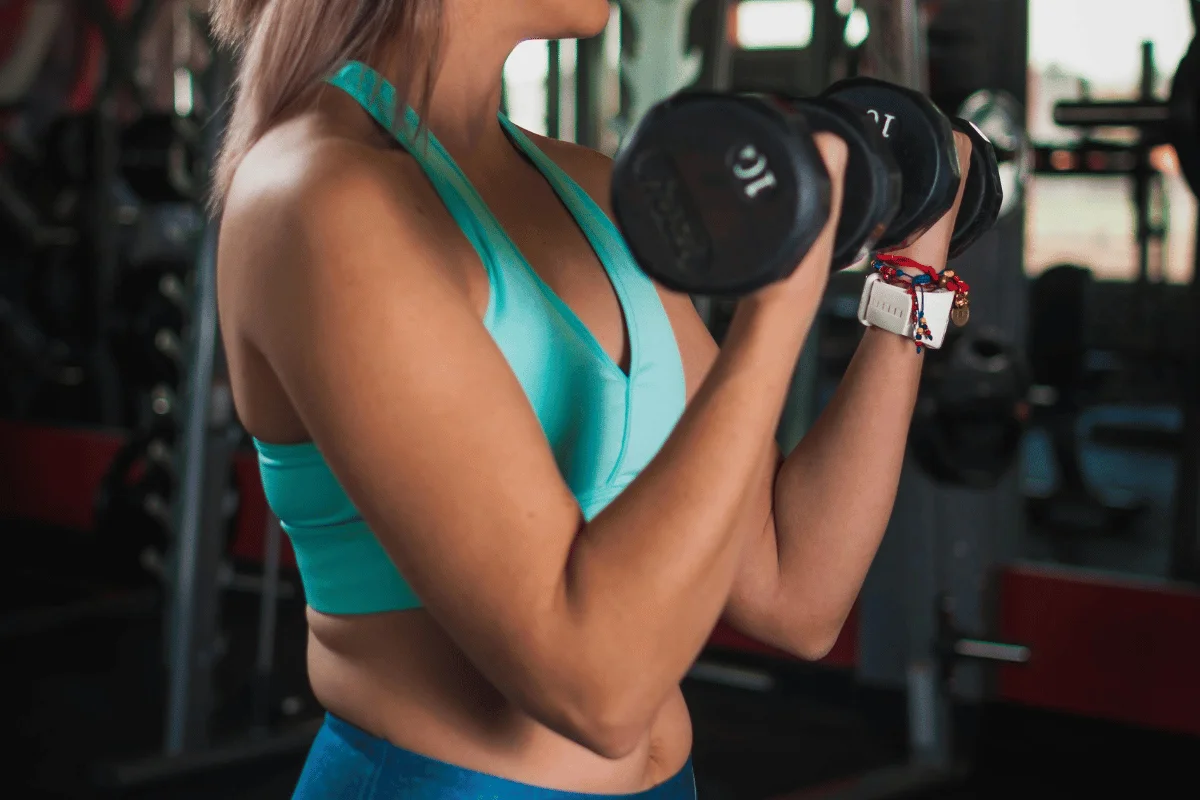 Woman in turquoise workout attire lifting a 10-pound dumbbell during her strength training session in the gym.