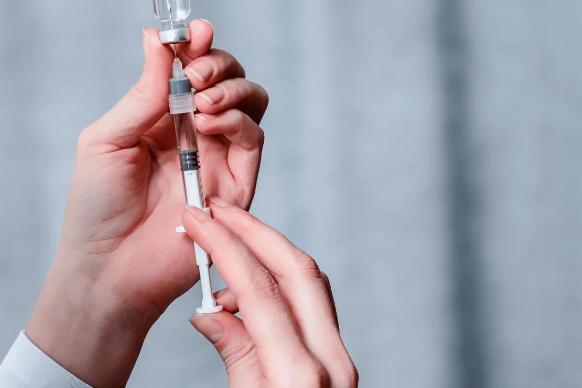 Close-up of hands filling a syringe with a vaccine or medication.