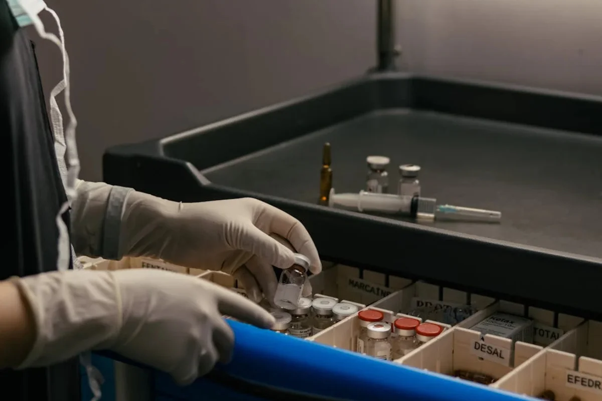 Person in lab coat handling medication vials in a tray.