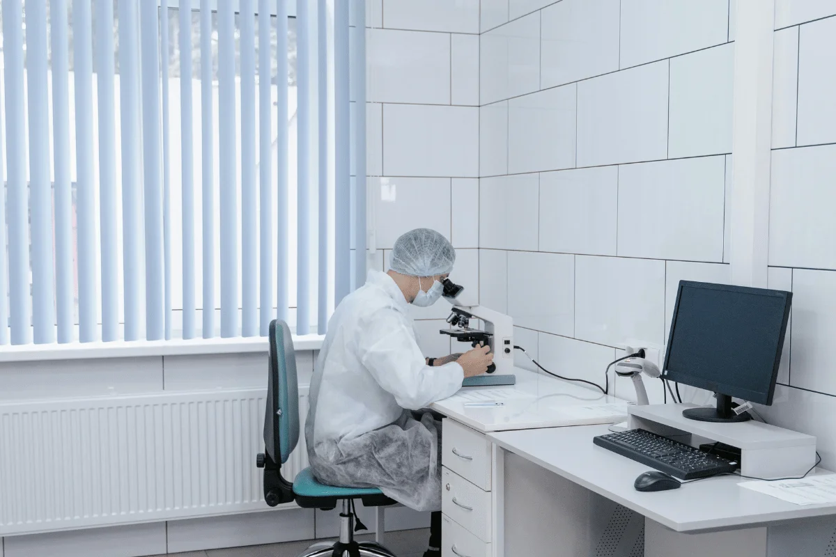 Lab technician analyzing samples using a microscope in a sterile environment.