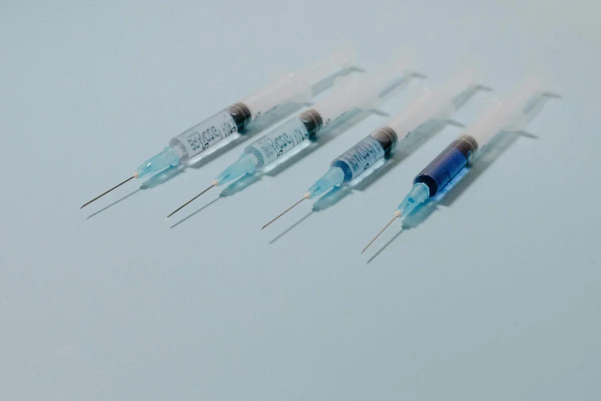 Four medical syringes with needles on a pale blue background.