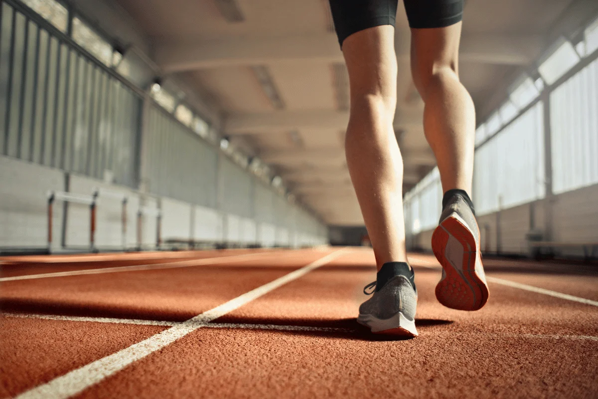 Close-up of a runner's legs walking on an indoor track during a workout session.