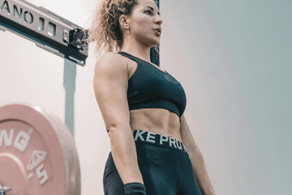 Woman in athletic wear standing near weightlifting equipment.