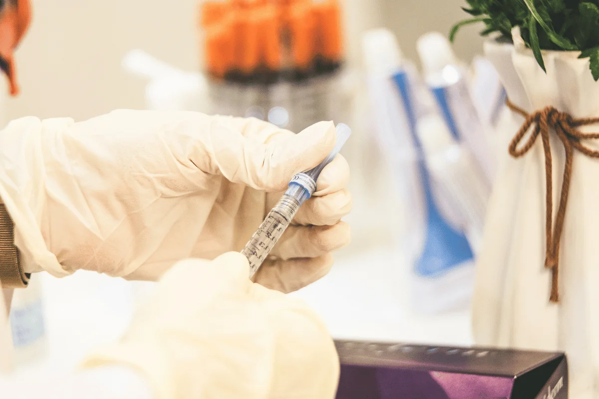 Medical professional wearing gloves holding a syringe filled with liquid.