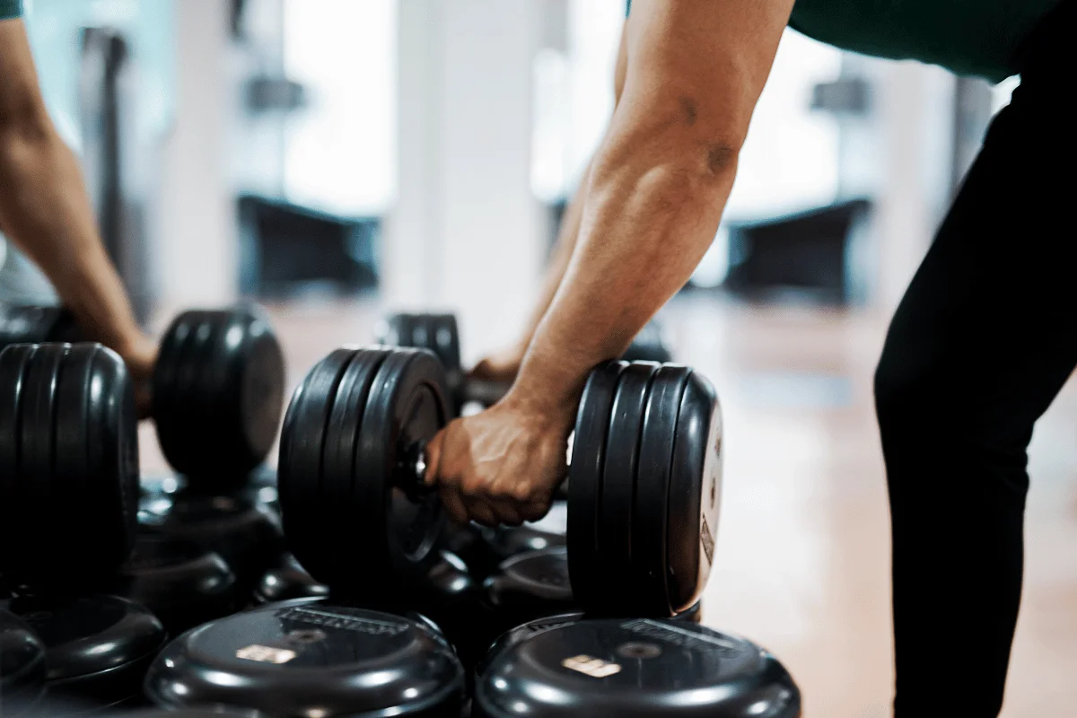 Person picking up a heavy dumbbell in a gym.