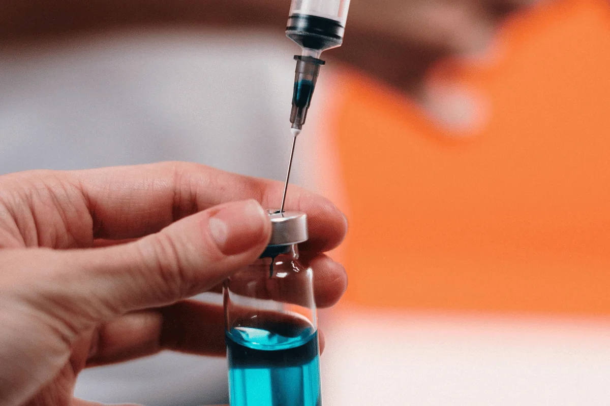 A person holding a syringe filled with blue liquid in a vial.