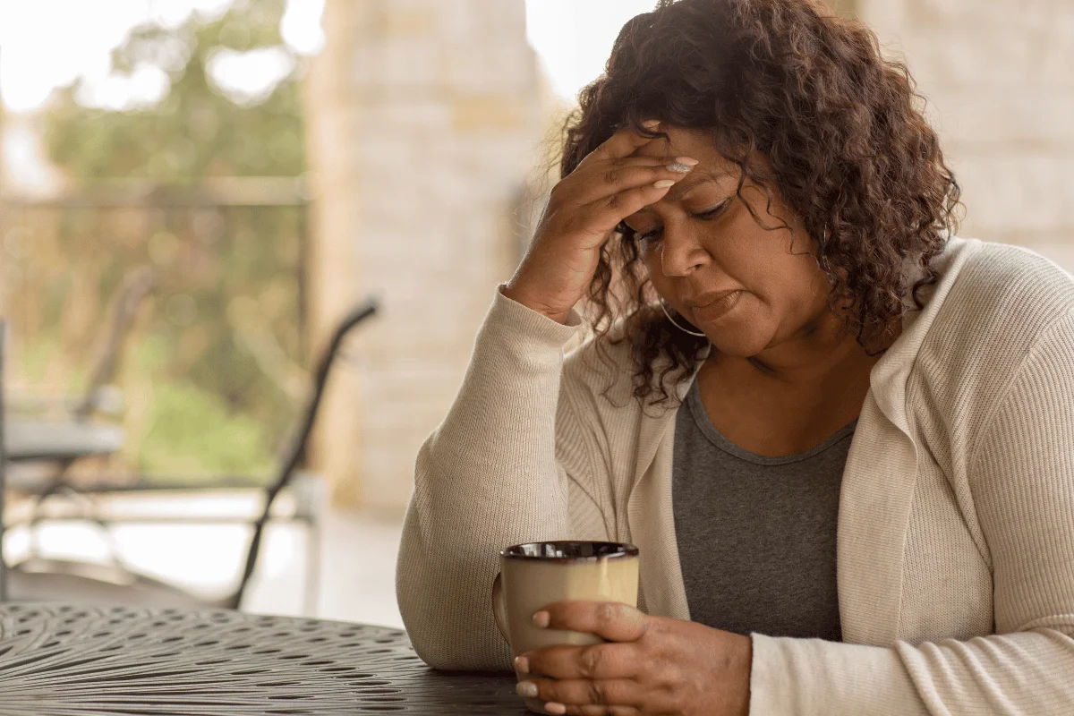 Person holding a cup at a patio table, with a blurred rectangle over their head.