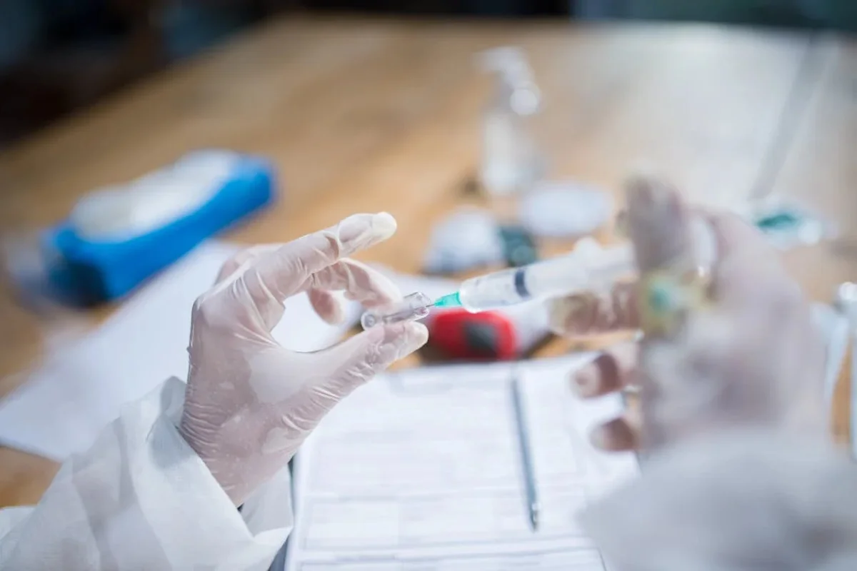 Close-up of hands in gloves handling a syringe and vial in a lab setting.