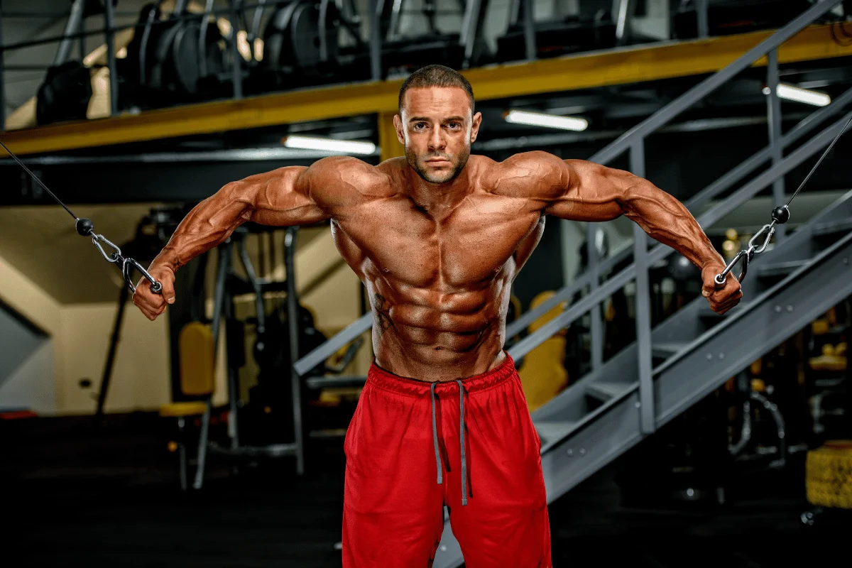 Muscular man performing cable crossover exercise, showcasing defined chest and arm muscles.