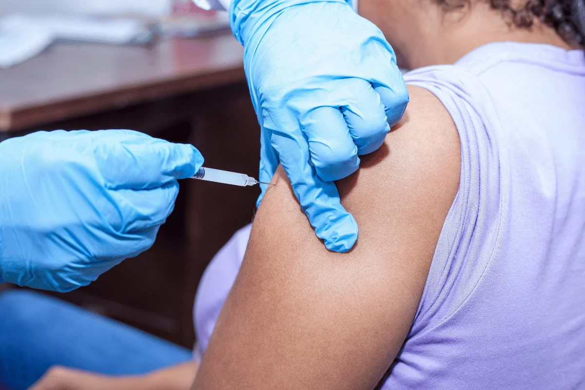 A person receiving an injection in their upper arm from a healthcare professional wearing blue gloves.