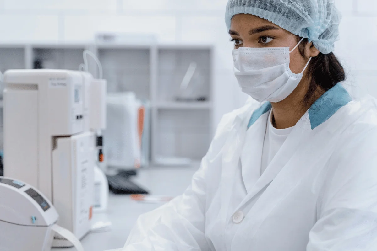 Medical professional in white lab coat with medical equipment in the background.