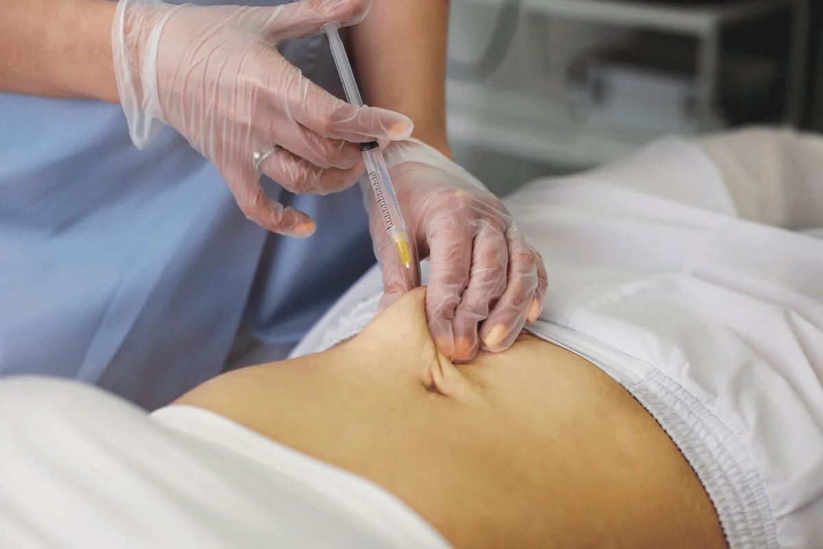 Medical professional administering an abdominal injection with a syringe.