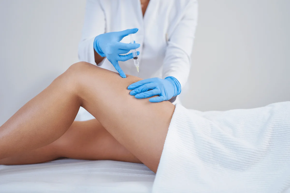 Medical professional administering an injection to a patient's thigh.