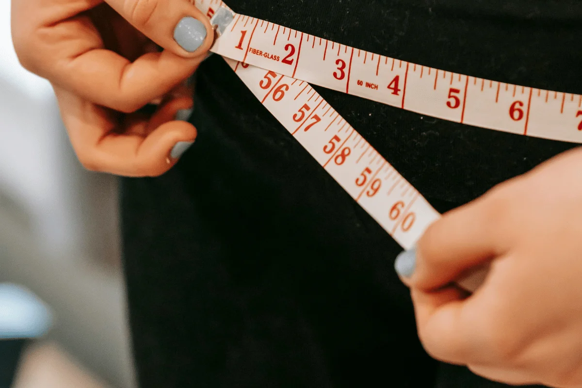 Close-up of a person measuring their waist with a flexible tape measure.