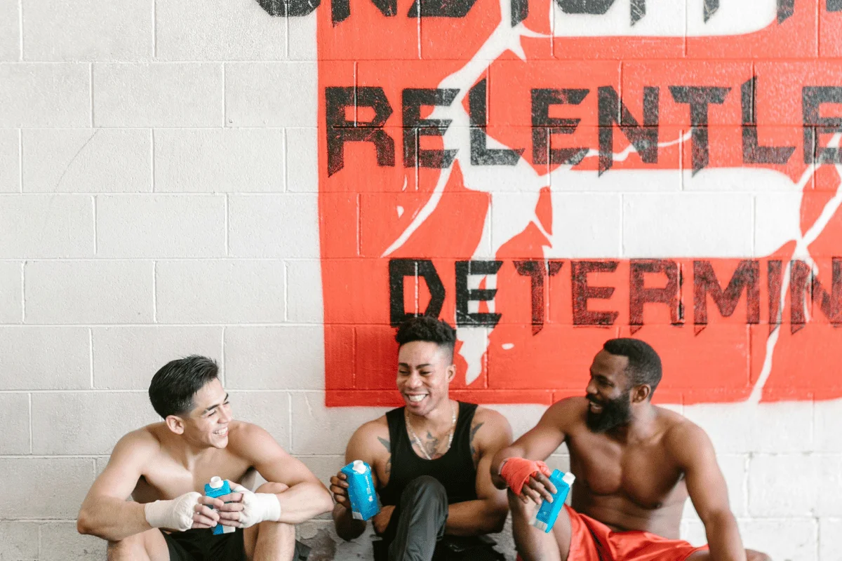 Three men taking a break from their workout in front of a gym mural.